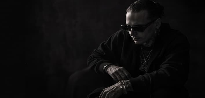 A man in sunglasses seated against a dark ground