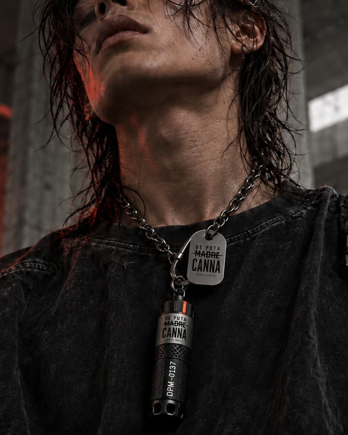 A titanium capsule and stamped tag hanging on a steel chain over a washed black tee, the wearer's head tipped back